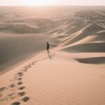 Person entfernt auf Sanddünenlandschaft im Licht tief stehender Sonne, im Vordergrund ihre Fußspuren im Sand
