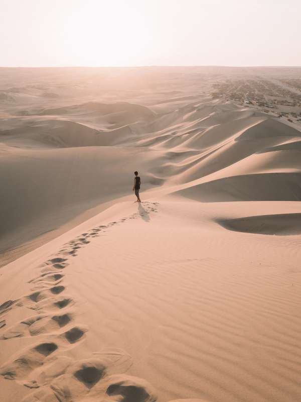 Person entfernt auf Sanddünenlandschaft im Licht tief stehender Sonne, im Vordergrund ihre Fußspuren im Sand