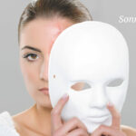 Eine Person sieht hinter einer schräg vor das Gesicht gehaltenen, weißen Maske hervor.