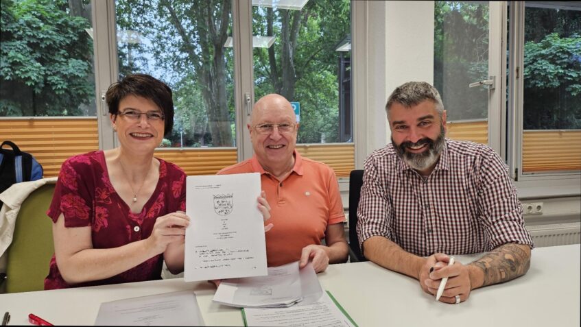 Gruppenfoto der Unterzeichnenden, Pfarrerin Schröder hält den unterschriebenen Vertag in die Kamera.