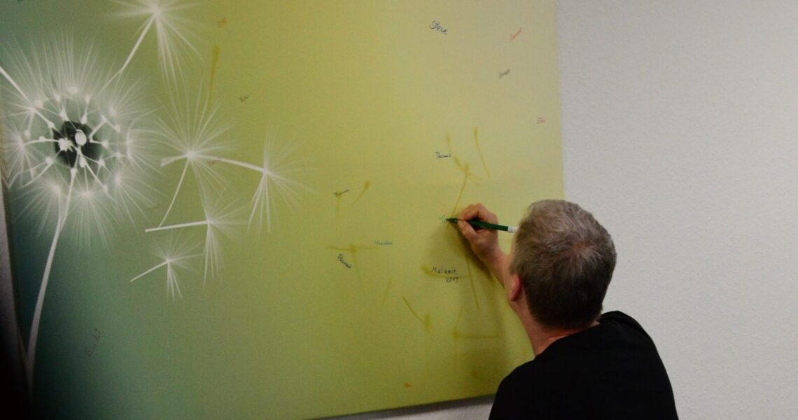 Eine Person schreibt den Namen eines Verstorbenen auf ein Bild mit Pusteblume