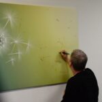 Eine Person schreibt den Namen eines Verstorbenen auf ein Bild mit Pusteblume