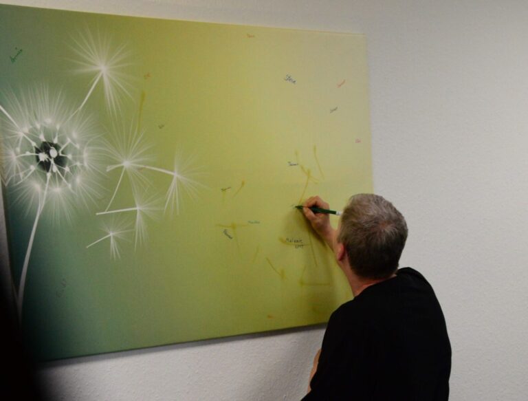 Eine Person schreibt den Namen eines Verstorbenen auf ein Bild mit Pusteblume