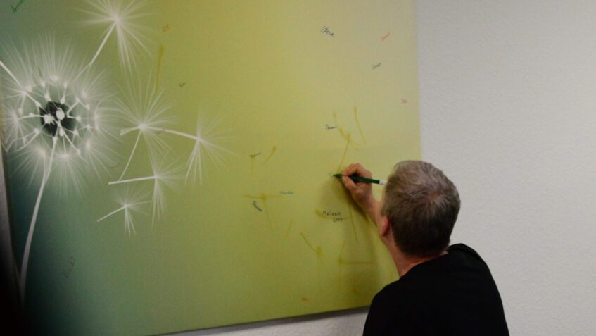 Eine Person schreibt den Namen eines Verstorbenen auf ein Bild mit Pusteblume