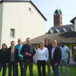 Gruppenfoto von Carsten Tag, Ute Engel, Samuel Mergenthal und den Mitarbeitenden der Flüchtlings- und Migrationsberatung des Diakonischen Werkes Hanau - Main-Kinzig vor dem Gebäude an der Christuskirche.
