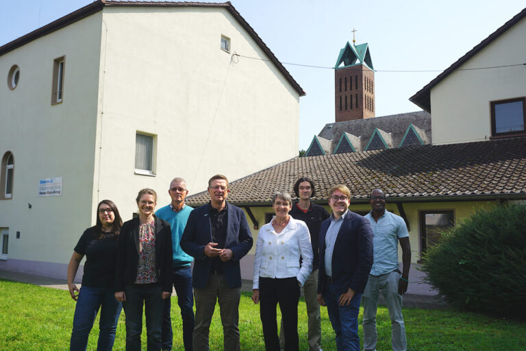 Gruppenfoto von Carsten Tag, Ute Engel, Samuel Mergenthal und den Mitarbeitenden der Flüchtlings- und Migrationsberatung des Diakonischen Werkes Hanau - Main-Kinzig vor dem Gebäude an der Christuskirche.