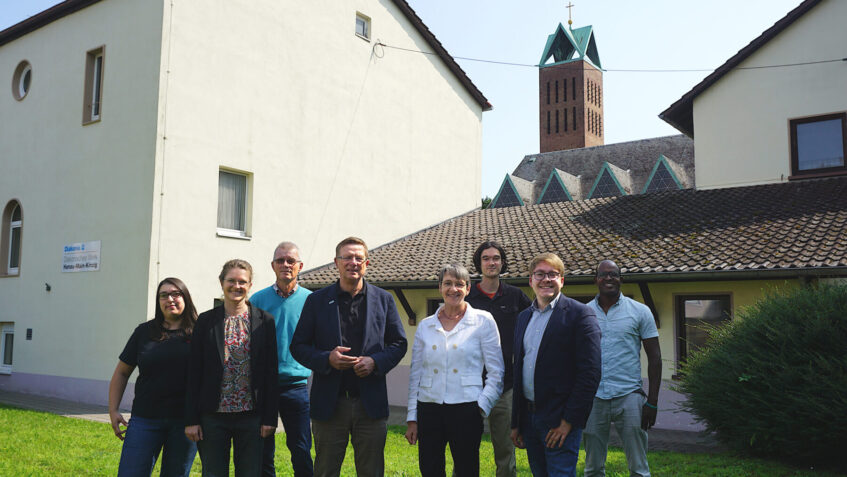 Gruppenfoto von Carsten Tag, Ute Engel, Samuel Mergenthal und den Mitarbeitenden der Flüchtlings- und Migrationsberatung des Diakonischen Werkes Hanau - Main-Kinzig vor dem Gebäude an der Christuskirche.