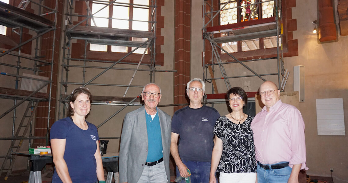 Gruppenfoto vor den Baugerüsten im Chorraum, ein erstes wieder eingebautes Buntglasfenster im Hintergrund