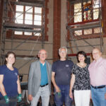 Gruppenfoto vor den Baugerüsten im Chorraum, ein erstes wieder eingebautes Buntglasfenster im Hintergrund