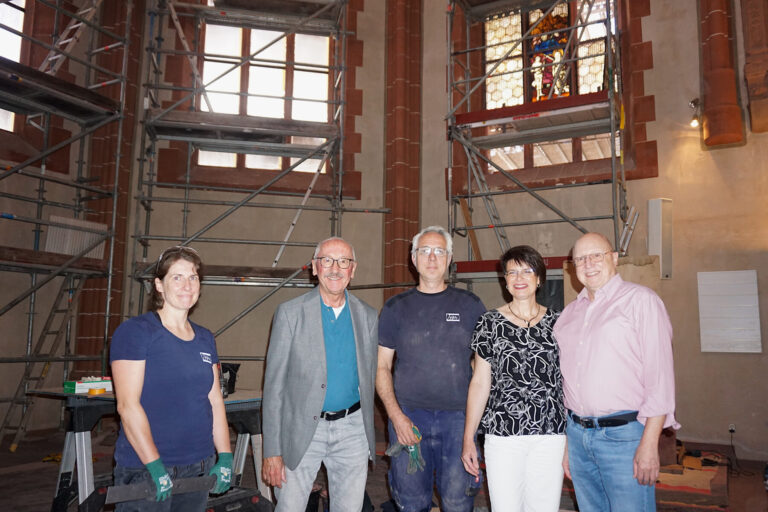 Gruppenfoto vor den Baugerüsten im Chorraum, ein erstes wieder eingebautes Buntglasfenster im Hintergrund