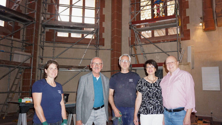 Gruppenfoto vor den Baugerüsten im Chorraum, ein erstes wieder eingebautes Buntglasfenster im Hintergrund