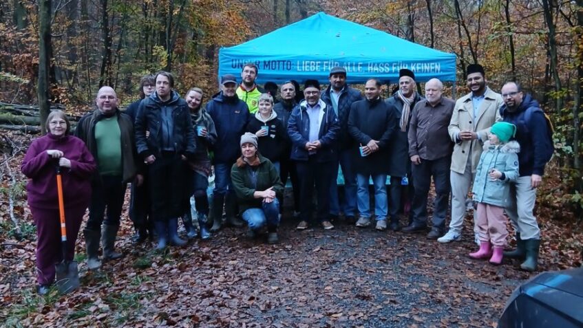 Gruppenfoto der Teilnehmenden der Baumpflanzaktion im Wald vor einem blauen Pavillon.