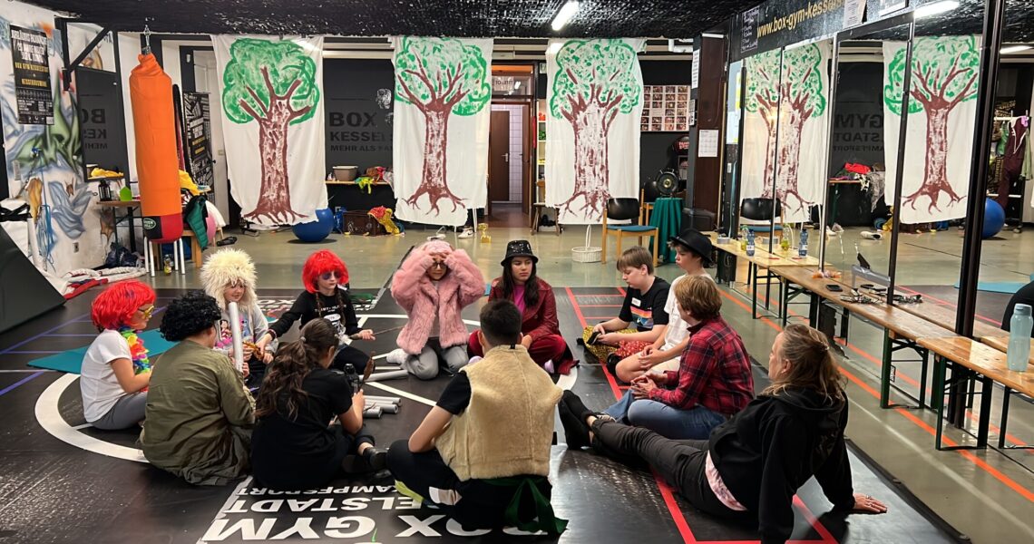 Die Kinder sitzen in Verkleidung im Kreis und besprechen etwas.