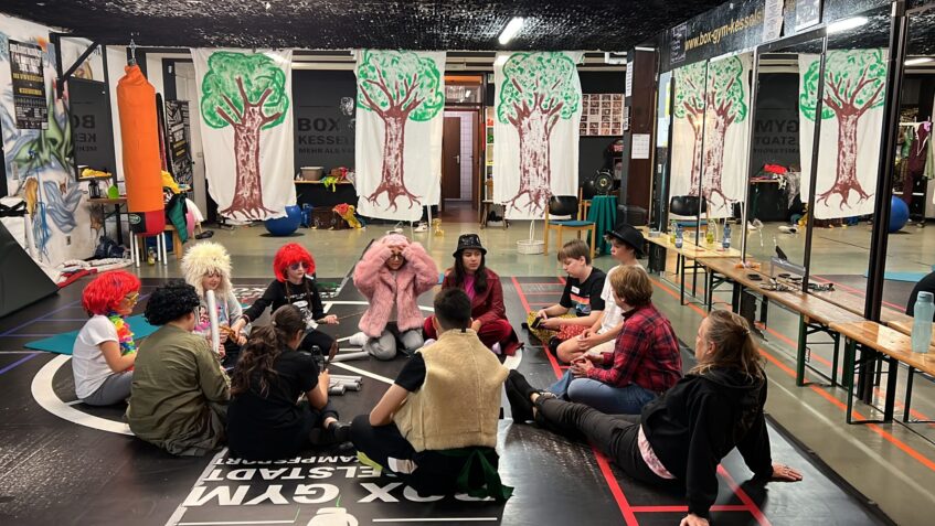 Die Kinder sitzen in Verkleidung im Kreis und besprechen etwas.