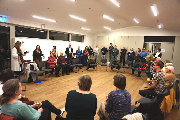 Personen stehen und sitzen in einem Kreis, die Vorsitzende des KV spricht zu den Anwesenden