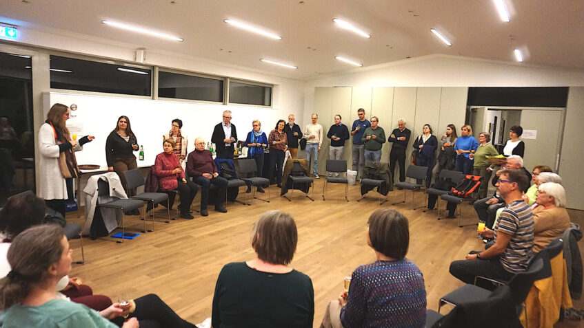 Personen stehen und sitzen in einem Kreis, die Vorsitzende des KV spricht zu den Anwesenden