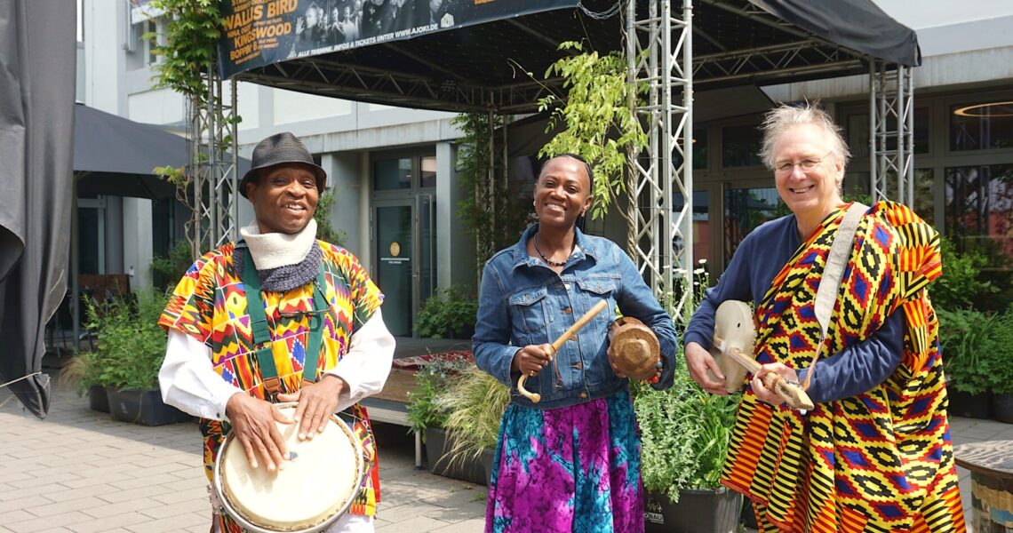 Drei Menschen in Afrikanischer Tracht mit landestypischen Musikinstrumenten vor der Alten Johanneskirche