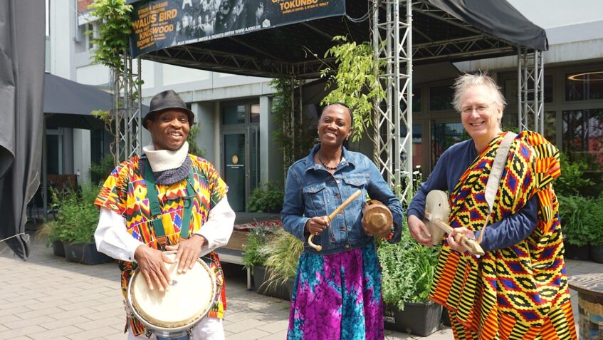 Drei Menschen in Afrikanischer Tracht mit landestypischen Musikinstrumenten vor der Alten Johanneskirche