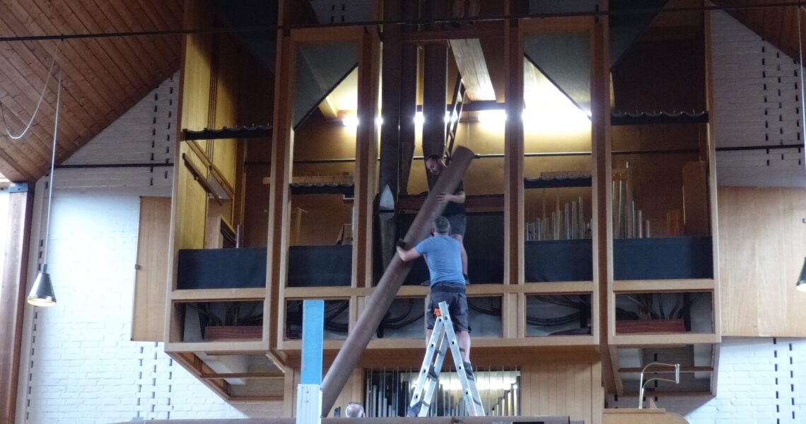 Zwei Männer bauen gemeinsam eine der großen Pfeifen der Peter-Orgel ab.