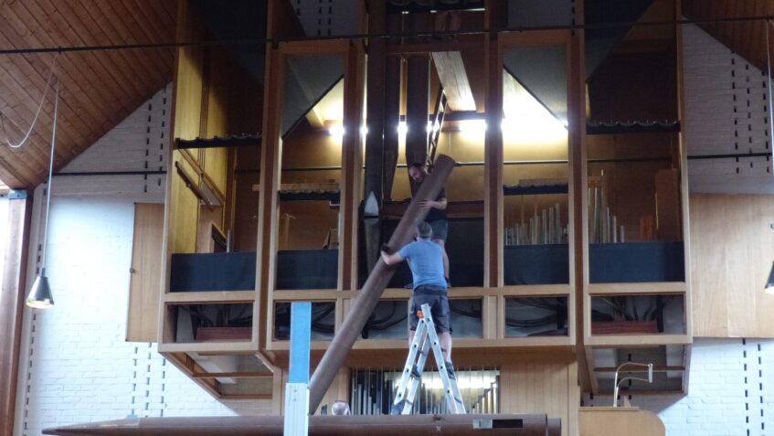 Zwei Männer bauen gemeinsam eine der großen Pfeifen der Peter-Orgel ab.
